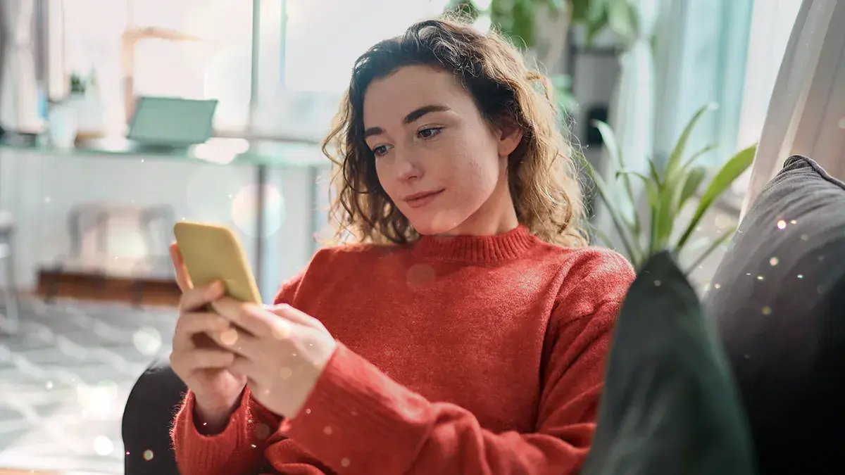 A woman on a sofa looks at her mobile phone. This is Virgin Media's guide to freeing up phone storage space.