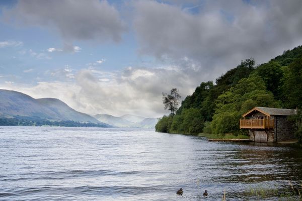 Lakeside scene with a wooden cabin on the right surrounded by trees