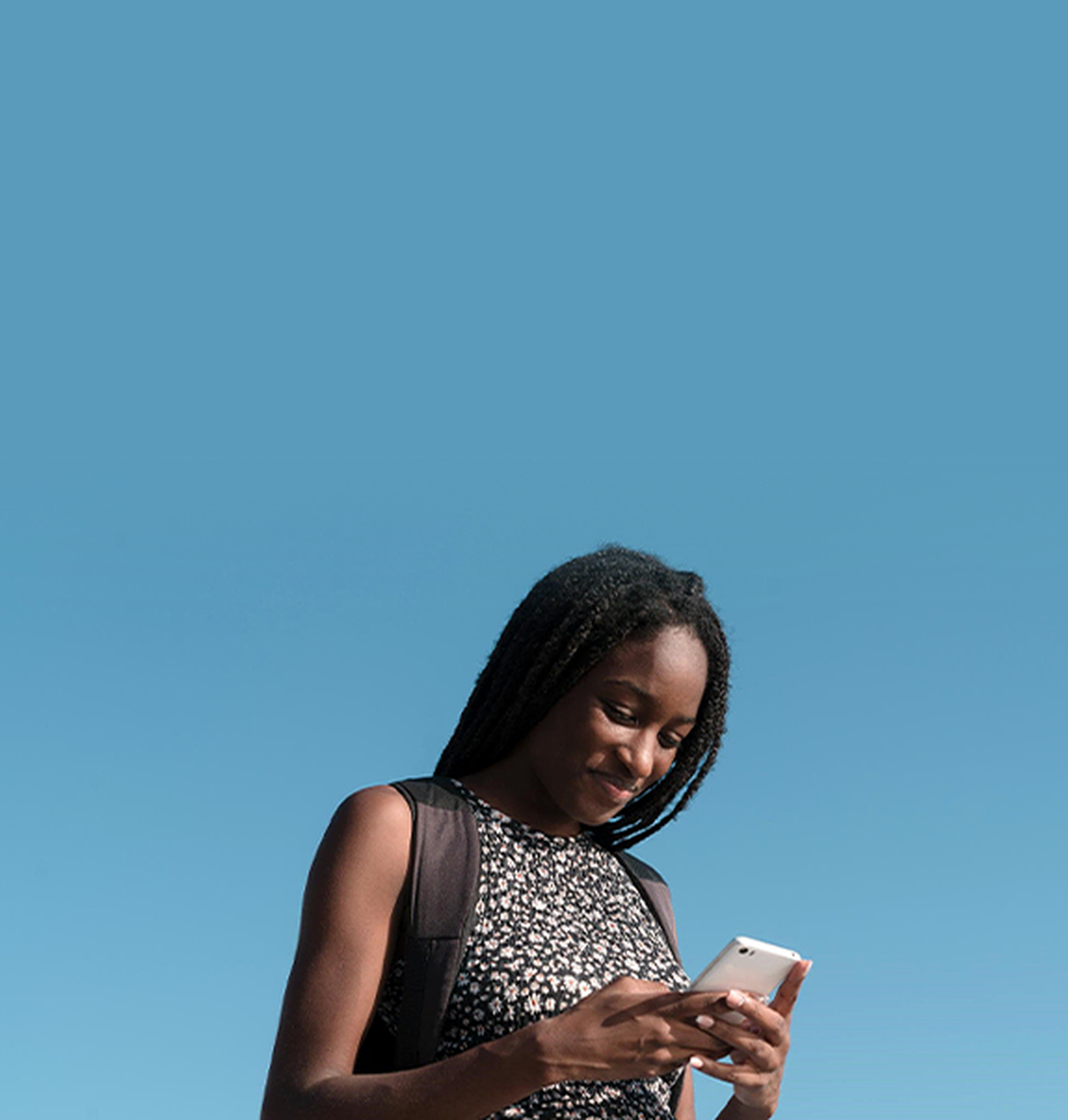 A lady with deadlocks looks down at her phone with a slight smile 