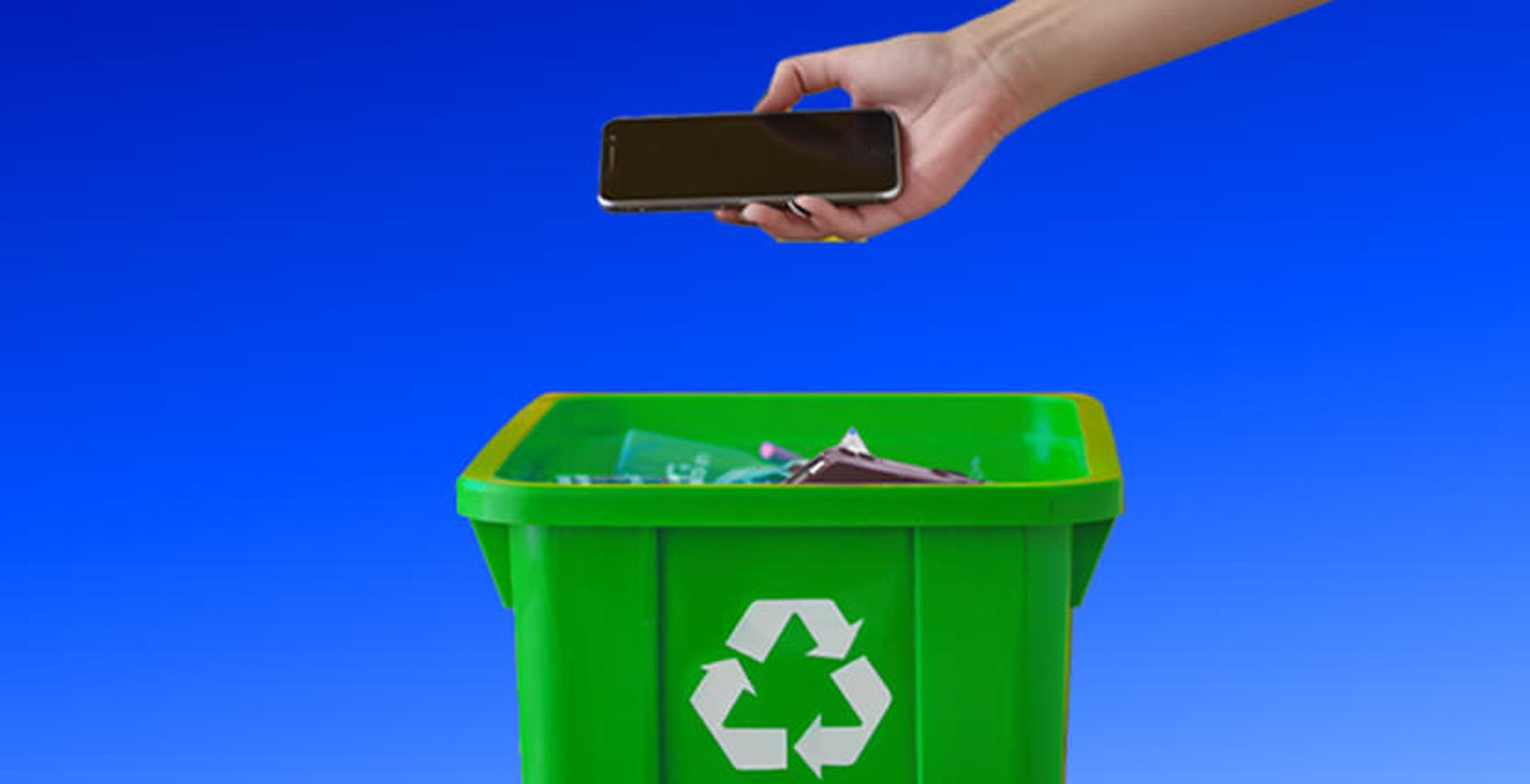 A hand holds a smartphone above a green recycling bin, symbolizing responsible e-waste disposal. Blue gradient background.
