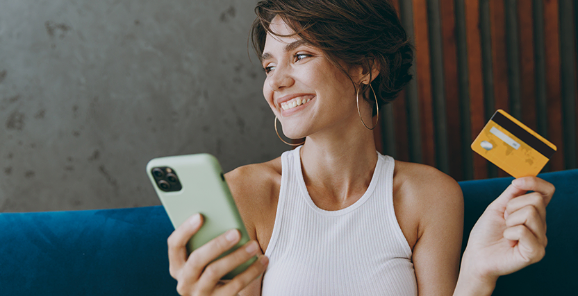 A smiling woman holds a smartphone and a credit card