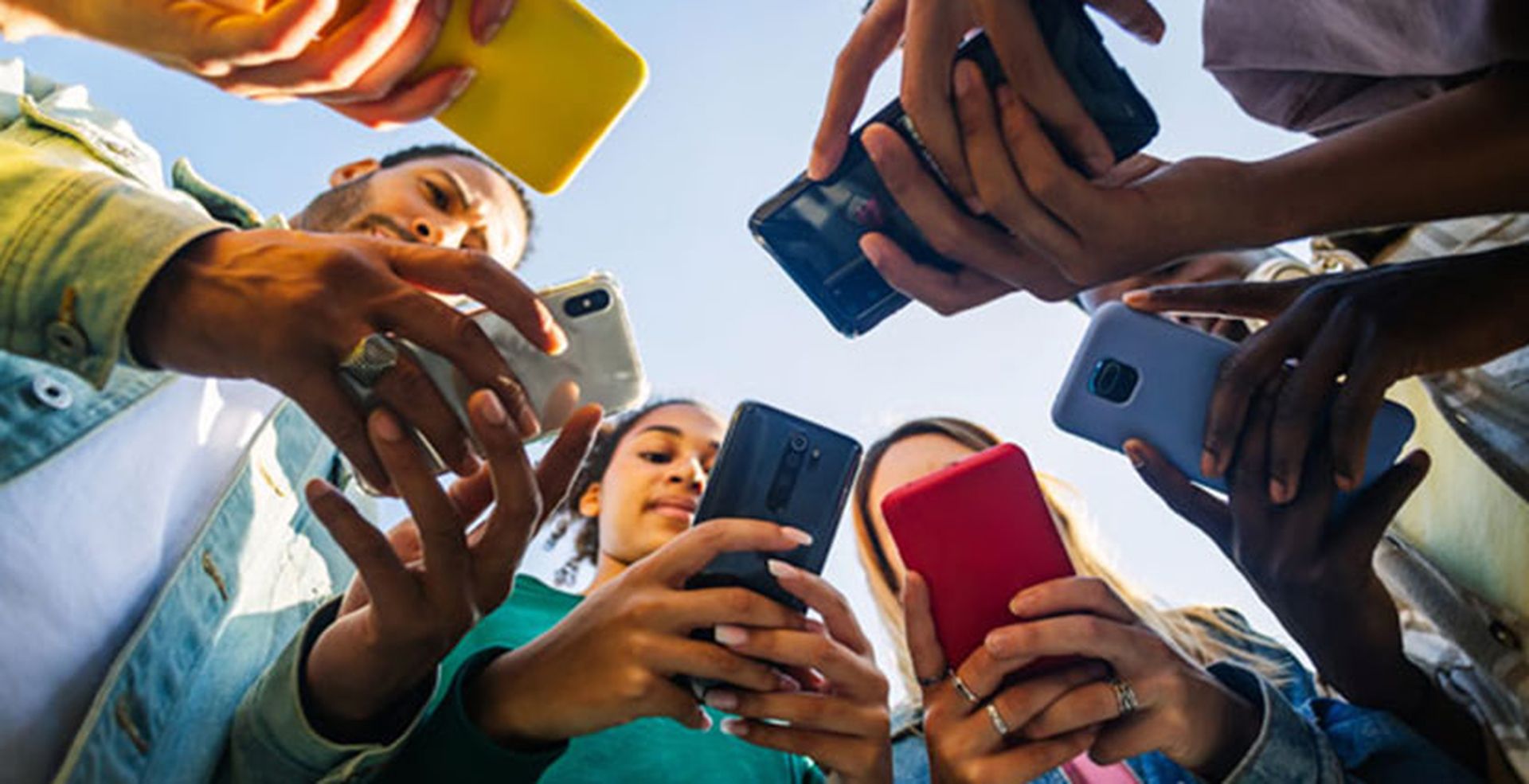 People standing in a circle looking down at smartphones, each holding a different colored case, against a clear blue sky.