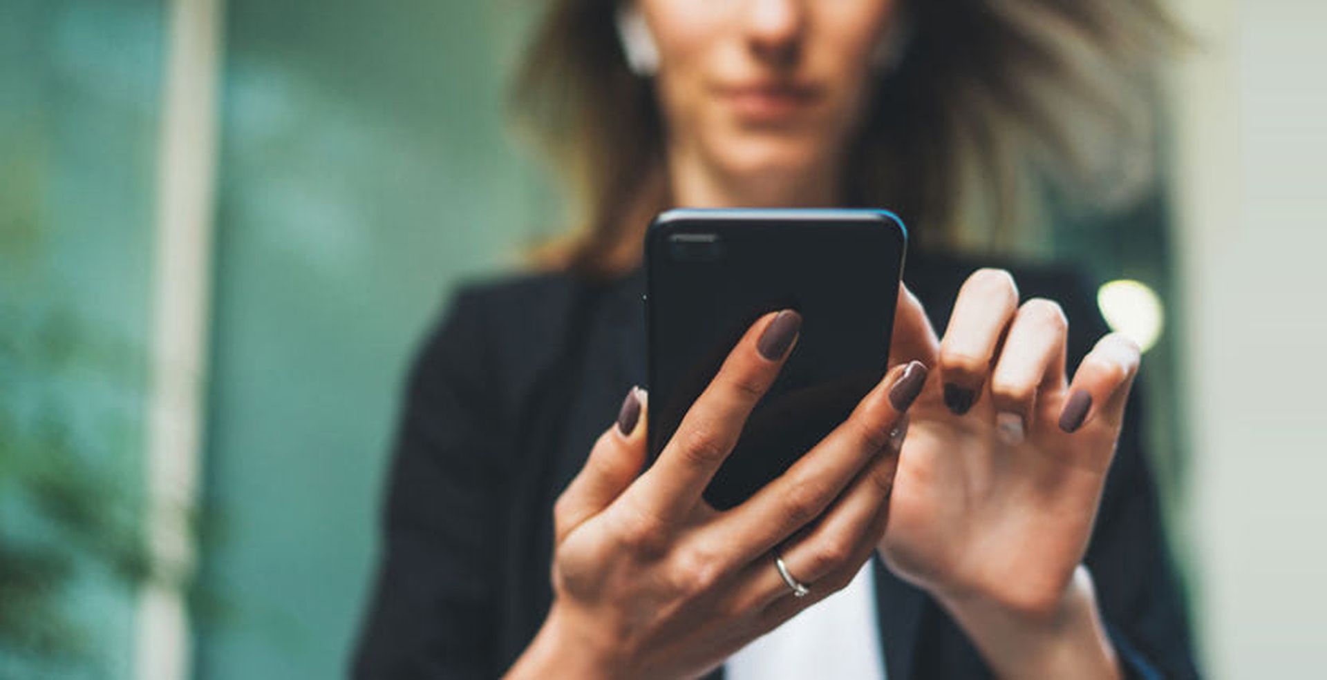 Person using a smartphone, wearing wireless earbuds, with blurred background. Focus on hands and device, showcasing modern technology use.