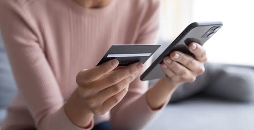 Person holding a smartphone and a credit card, preparing for an online transaction while seated on a couch.