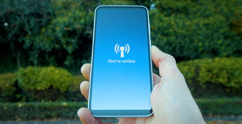 A hand holding a smartphone displaying the message "You're online" with a wireless icon, set against a blurred outdoor background of greenery.