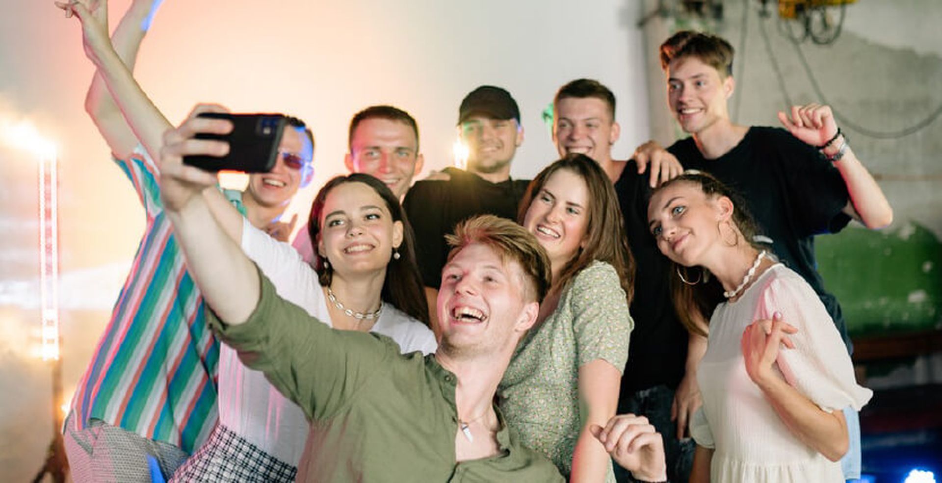A group of eight young people smiling and posing for a selfie at a lively indoor gathering.