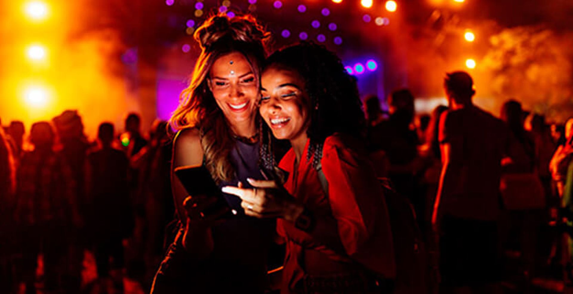 Two women at a night festival smiling at a smartphone