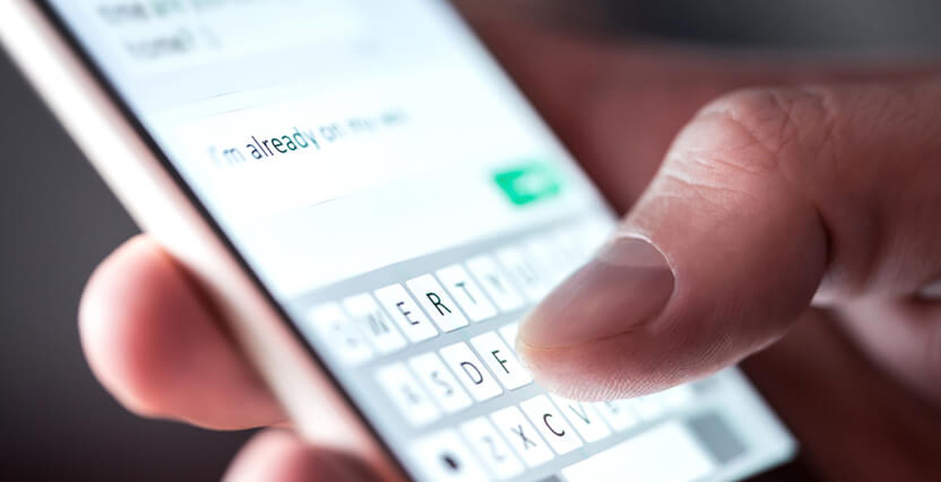 Close-up of a hand typing on a smartphone touchscreen, entering a text message that reads, "I'm already on my way."