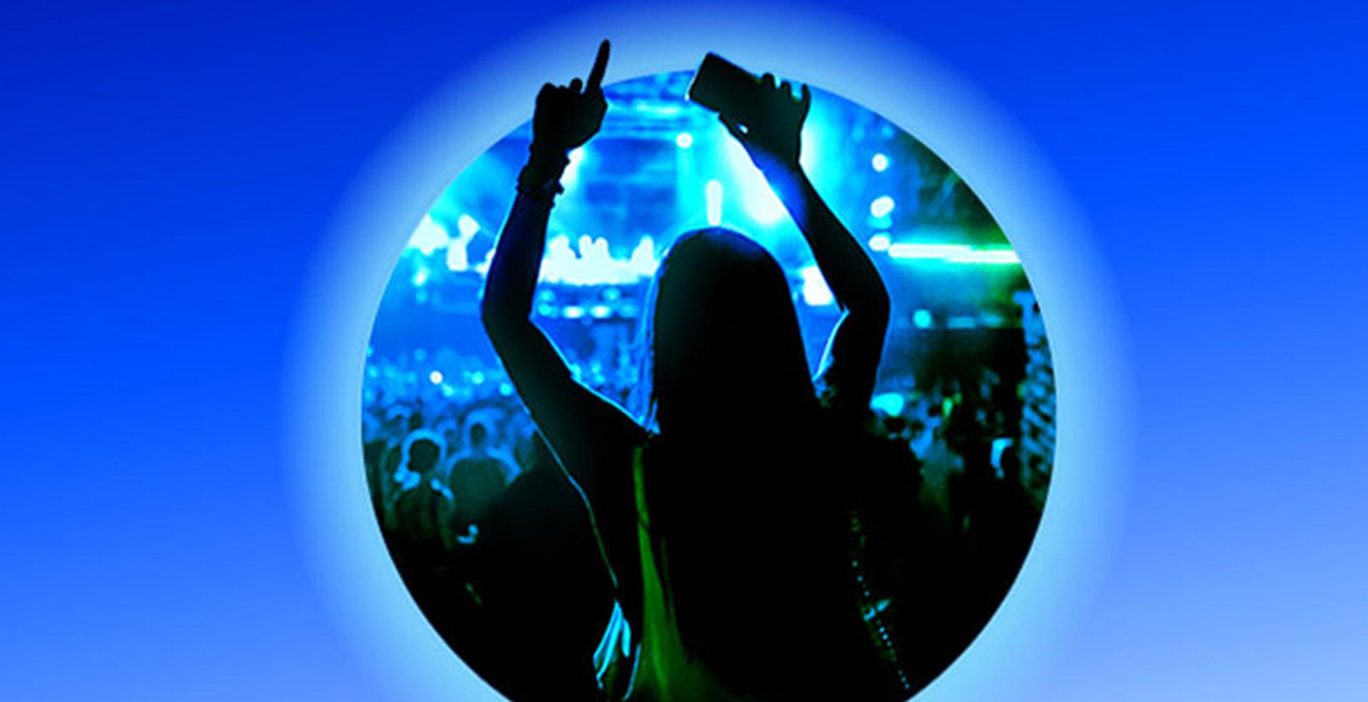 Silhouette of a concertgoer holding up a phone with hands raised in a blue-green lit crowd, framed in a circular vignette on a gradient blue background.