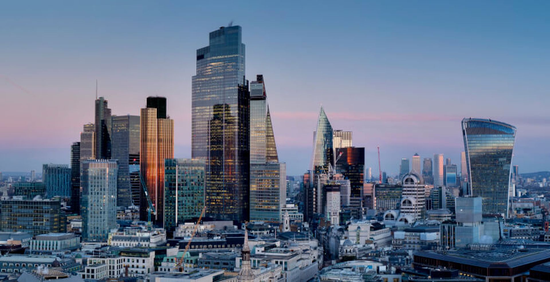 Skyline of London at dusk with modern skyscrapers and historic buildings under a clear blue sky.