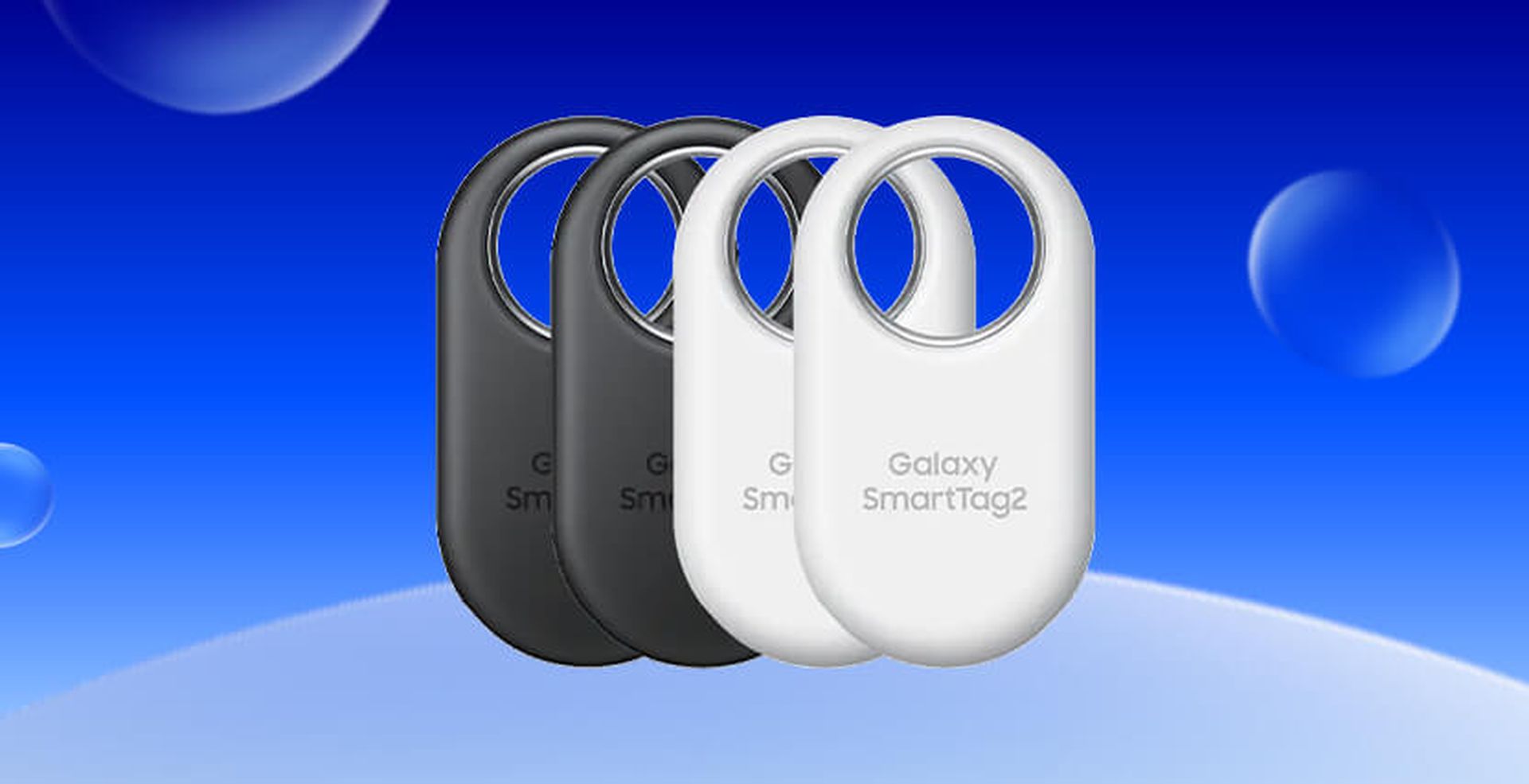 Four Galaxy SmartTag2 devices, two black and two white, against a blue background with bubble-like circles.
