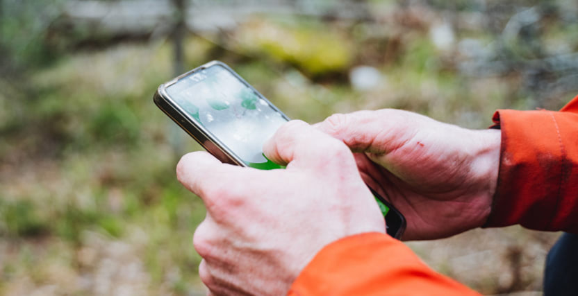Person in an orange jacket using a smartphone outdoors, with a blurred natural background.